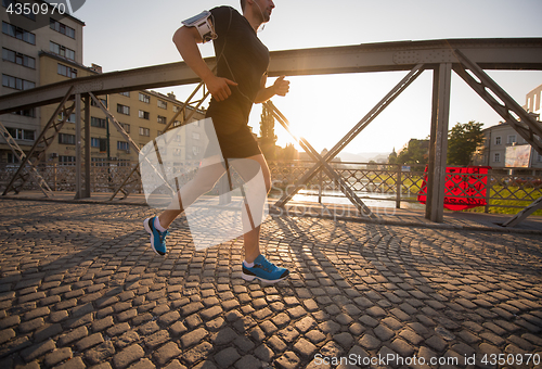 Image of man jogging across the bridge at sunny morning