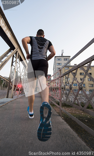 Image of man jogging across the bridge at sunny morning