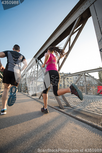 Image of young couple jogging across the bridge in the city