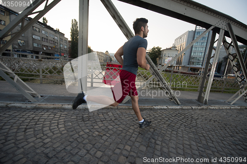 Image of man jogging across the bridge at sunny morning