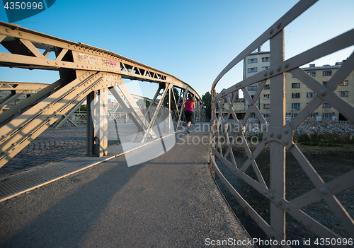 Image of woman jogging across the bridge at sunny morning