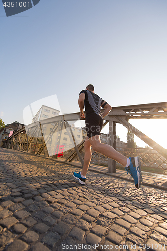 Image of man jogging across the bridge at sunny morning