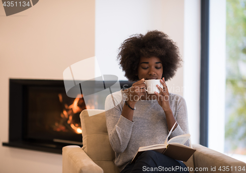 Image of black woman reading book  in front of fireplace