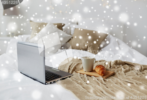 Image of laptop, coffee and croissant on bed at cozy home