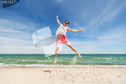 Image of smiling young man jumping on summer beach