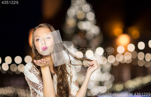 Image of happy woman sending air kiss over christmas lights