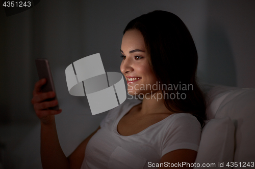 Image of happy young woman with smartphone in bed at night