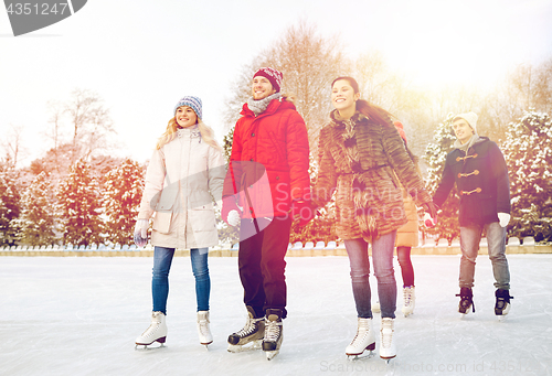 Image of happy friends ice skating on rink outdoors