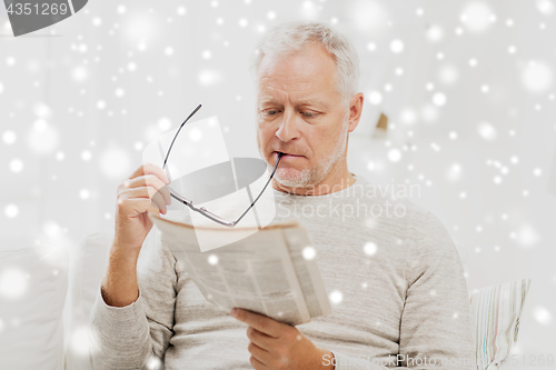 Image of senior man in glasses reading newspaper at home