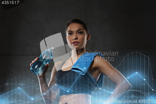 Image of woman with towel drinking water from bottle in gym