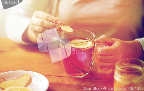 Image of close up of woman adding ginger to tea with lemon