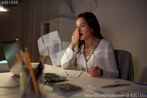 Image of tired woman with papers yawning at night office