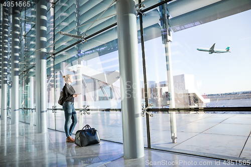 Image of Young woman waiting at airport, looking through the gate window.