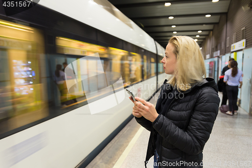 Image of Woman with a cell phone waiting for metro.