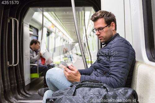 Image of Male commuter reading from mobile phone screen in metro.