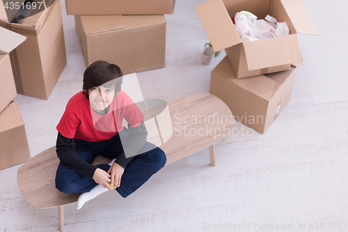 Image of boy sitting on the table with cardboard boxes around him top vie