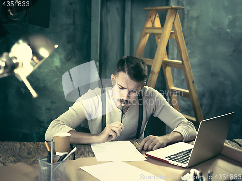 Image of Portrait of a bearded businessman who is working with his notebook at loft studio.