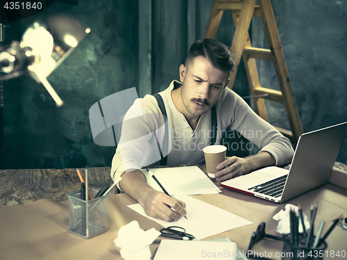 Image of Portrait of a bearded businessman who is checking details of his upcoming meeting in his notebook and typing.