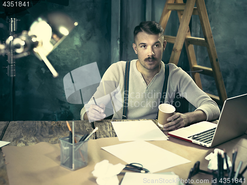Image of Portrait of a bearded businessman who is working with his notebook at loft studio.