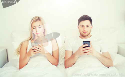 Image of couple with smartphones in bed