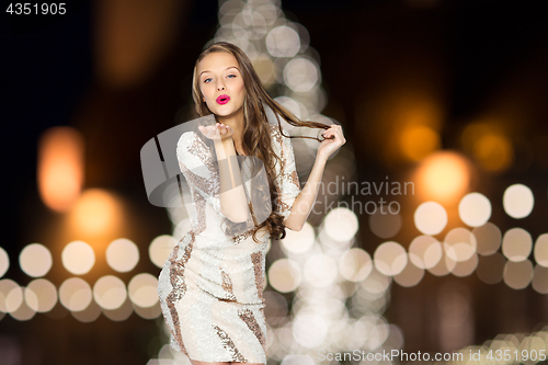 Image of happy woman sending air kiss over christmas lights