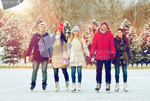 Image of happy friends ice skating on rink outdoors