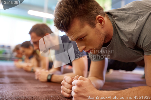 Image of man doing plank exercise at group training in gym