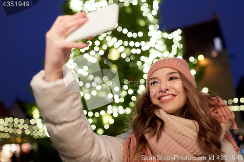 Image of young woman taking selfie over christmas tree