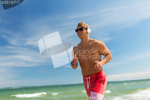 Image of happy man with headphones running along beach