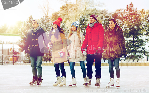 Image of happy friends ice skating on rink outdoors