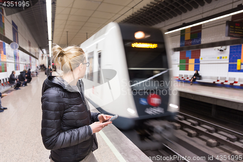 Image of Woman with a cell phone waiting for metro.