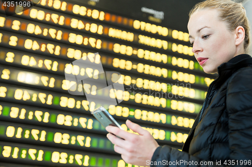 Image of Woman at airport in front of flight information board checking her phone.