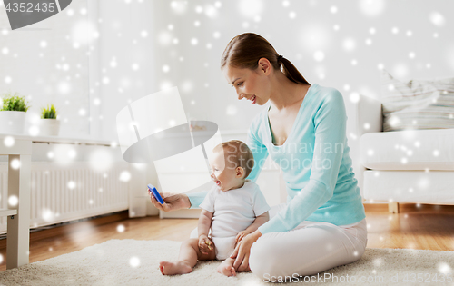 Image of happy mother showing smartphone to baby at home