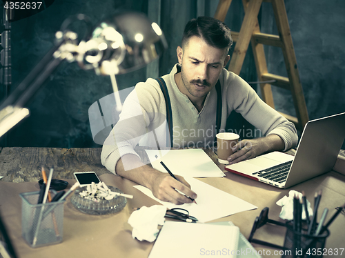 Image of The handsome elegant man sitting at home table, working and using laptop while smoking cigarettes