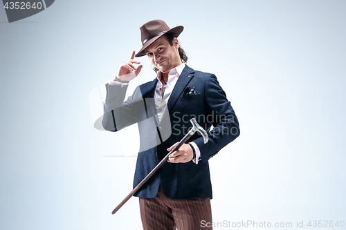 Image of The mature man in a suit and hat holding cane.