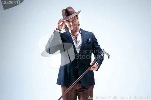 Image of The mature man in a suit and hat holding cane.