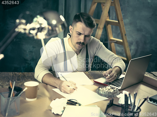 Image of The handsome elegant man sitting at home table, working and using laptop while smoking cigarettes