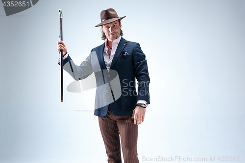 Image of The mature man in a suit and hat holding cane.