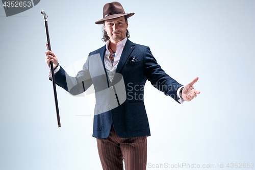 Image of The mature man in a suit and hat holding cane.