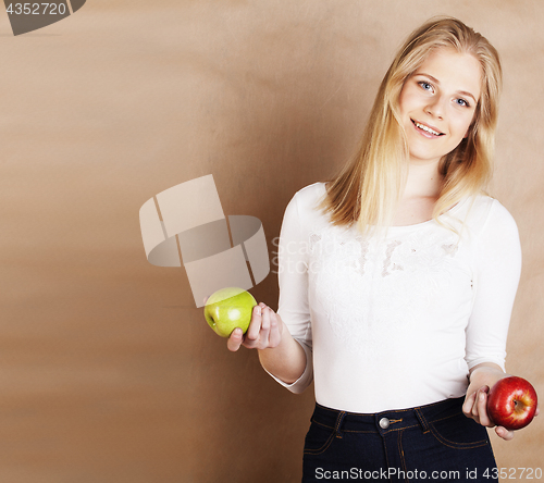 Image of young pretty blond woman with green apple happy cheerful smiling close up on warm brown background, lifestyle real people concept