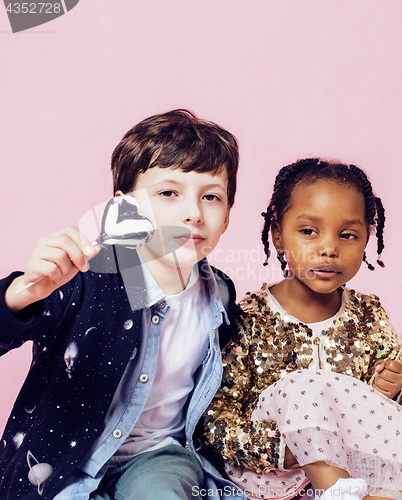 Image of lifestyle people concept: diverse nation children playing together, caucasian boy with african little girl holding candy happy smiling 