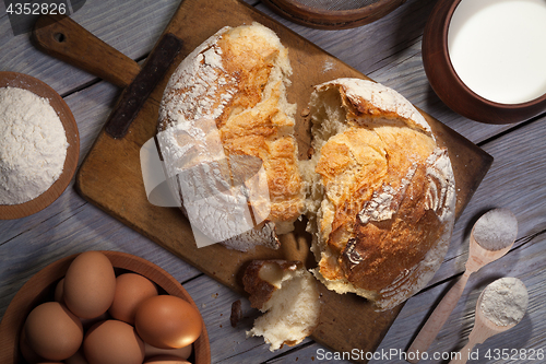 Image of Torned homemade bread loaf on old cutting board with cooking ingredients.