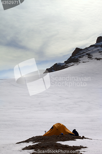 Image of Hiker sitting near camping tent in evening snow mountains