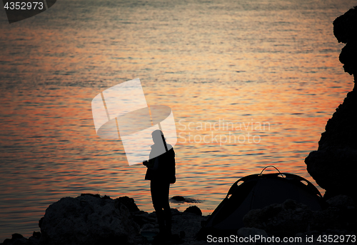 Image of Silhouette of trekker on rocky seashore near camping tent on ove