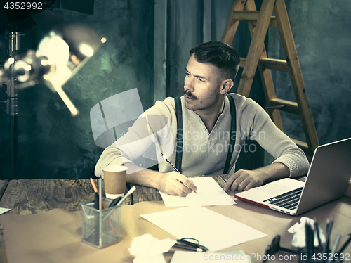 Image of Portrait of a bearded businessman who is working with his notebook at loft studio.