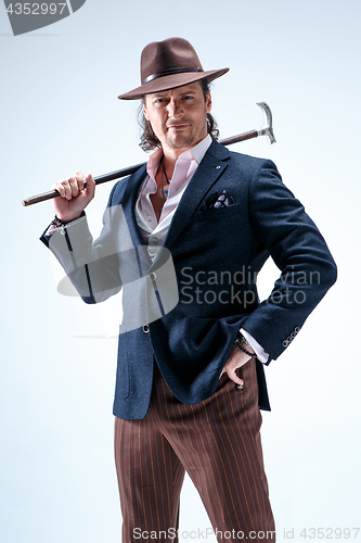 Image of The mature man in a suit and hat holding cane.