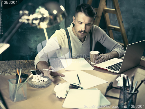 Image of The handsome elegant man sitting at home table, working and using laptop while smoking cigarettes