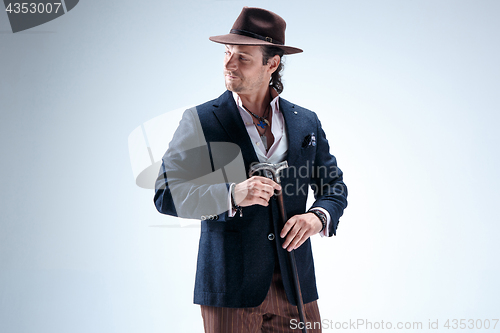 Image of The mature man in a suit and hat holding cane.