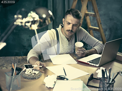 Image of The handsome elegant man sitting at home table, working and using laptop while smoking cigarettes