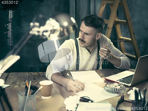 Image of The handsome elegant man sitting at home table, working and using laptop while smoking cigarettes